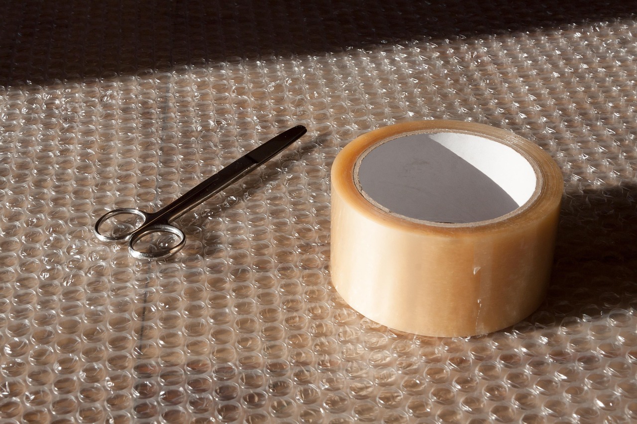 A roll of brown packing tape and scissors lying on bubble wrap
