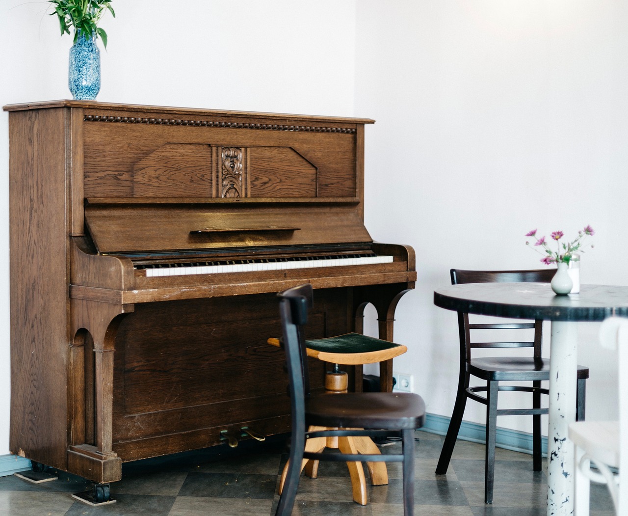 A wooden upright piano against a white wall beside a small table